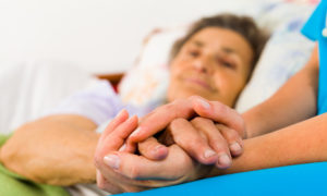 woman in bed holding hands with care partner